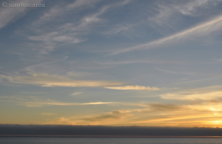 sunset on the Pacific Ocean with stripes of clouds and fog at the horizon